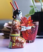 Kleine kniende, chinesische Figur trägt eine Orchideenblüte