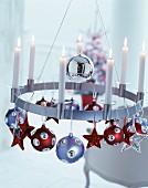 Lit white candles in modern, metal candle wreath decorated with Christmas baubles