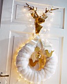 Festive arrangement of white wreath, fairy lights and shiny gold stag's head on door