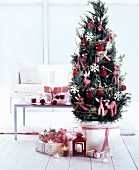 Eingepflanztes Bäumchen mit rotweiß karierten Stofftieren und roten Weihnachtskugeln dekoriert, daneben verpackte Geschenke