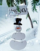 Wooden snowman with labelled sign hung from fir branch