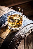 Ein Glas Whiskey mit Eis auf altem Holzfass