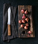 Small red onions on a wooden board and an old knife on a fabric napkin