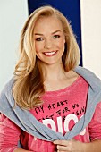 A young blonde woman wearing a pink printed T-shirt with a jumper over her shoulders