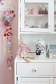 Rabbit soft toy on romantic, white dresser next to hair clips clipped on ribbon hung on wall in girl's bedroom
