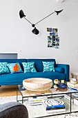 Designerlampe an der Wand über blauem Sofa, filigraner Couchtisch