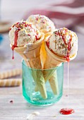 Three cones of vanilla ice cream with strawberry sauce and sugar sprinkles in a light blue glass
