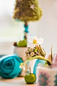 Hellebore flowers, green apple, turquoise felt flower and small tree ornament in blurred background