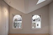 Blick auf zwei Rundbogenfenster in modernisiertem kahlem Raum mit raumhohem schlichtem Einbauschrank