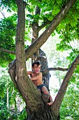 A little boy wearing bathing suits climbing a tree
