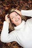 Smiling woman lying on autumn leaves