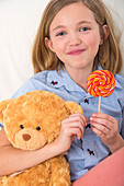 Girl holding lollypop and teddy bear