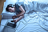 Man asleep in bed with laptop and phone