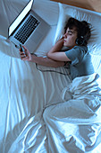 Man asleep in bed with laptop and phone