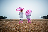 Two girls on beach holding umbrellas