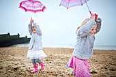 Two girls on beach holding umbrellas
