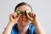 Boy holding cucumber over eyes