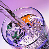 Water streaming into glass,mauve background