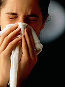Teenager with a common cold sneezing into a tissue
