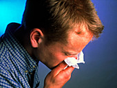 Young man with a cold blowing his nose