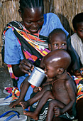 Mother feeding milk to malnourished child