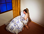 Fearful woman clutching a duvet in a corner