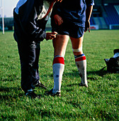 Physiotherapist treating player for leg cramp