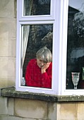 Depressed elderly woman stares through a window