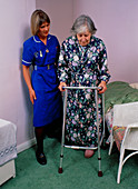 District nurse helps old woman use walking frame