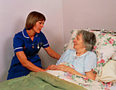 District nurse talks to elderly bedridden patient