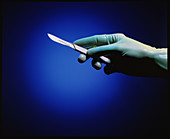 Gloved hand holding a medical scalpel