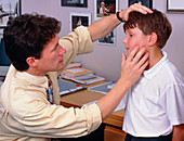Doctor examines young boy's face and neck