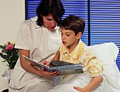 Paediatric nurse reads with a young boy in a ward