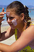 Girl at the beach applying sunblock facecream