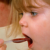 Sick young girl is fed a spoon of medicine