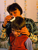 Woman using an electronic nit comb on a boy's head