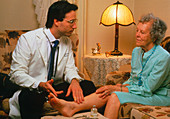 Home-visit doctor examines ankle of elderly woman