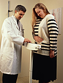Doctor monitors woman's weight on a weight scale