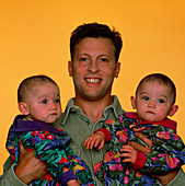 Infant identical twins being held by proud father