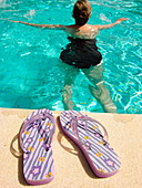 Flip-flops and woman swimming in pool