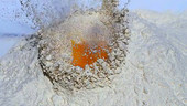 Egg yolk falling into flour