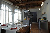 Modern, open-plan kitchen below rustic wood-beamed ceiling in renovated country house