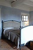 Double bed against blue-grey wall below white-painted wood-beamed ceiling