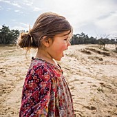 A little girl standing on sand dunes wearing a floral-patterned dress