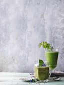 Two green smoothies garnished with borage and carrot leaves