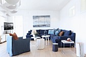 Maritime lounge area with white wood-clad walls, dark blue corner sofa, white side tables and TV