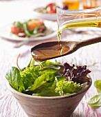Oil being pored over salad from a wooden spoon