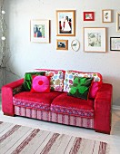 Romantic mixture of patterns on red sofa below framed pictures on wall