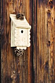 Traditional bird nesting box decorated with ornamental trim and pine cones hung on board wall