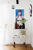 Vintage Servierwagen mit Flaschensammlung und Aufbewahrungsboxen vor Wand mit Frauenportrait